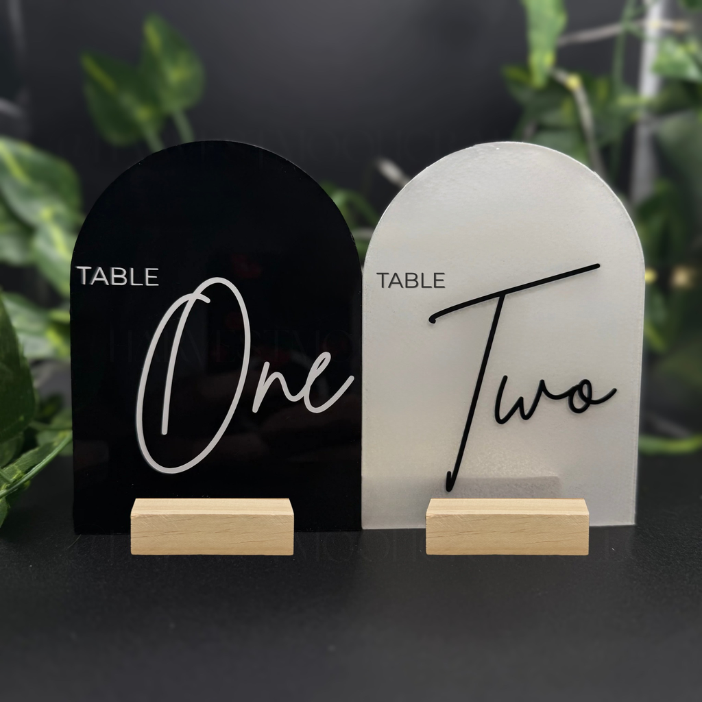 Two table number signs, one black and one white, with wooden stands on a dark background.