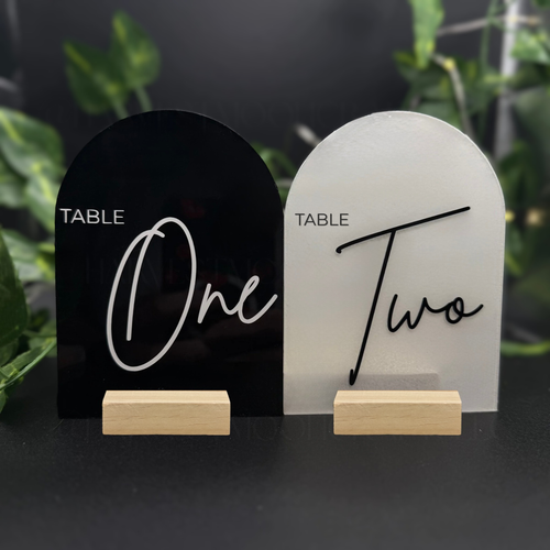 Two table number signs, one black and one white, with wooden stands on a dark background.